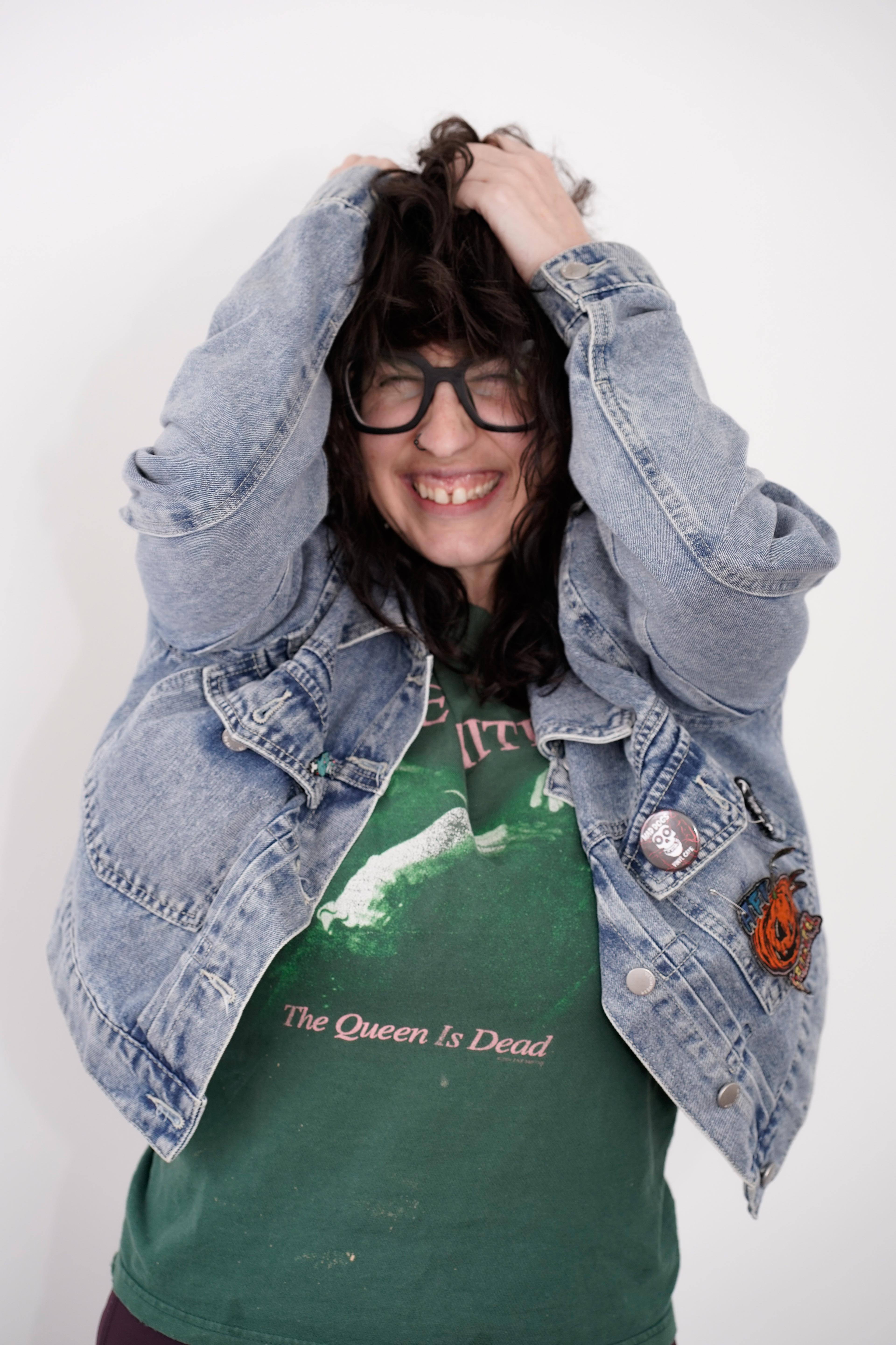 Dani Spinosa smiling, hands in hair, wearing a denim jacket